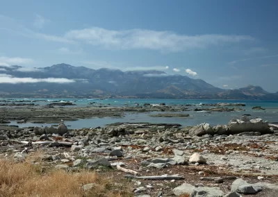 Rocky Kaikoura beach and turquoise sea with the cloudy Seaward Kaikoura Range in the background.